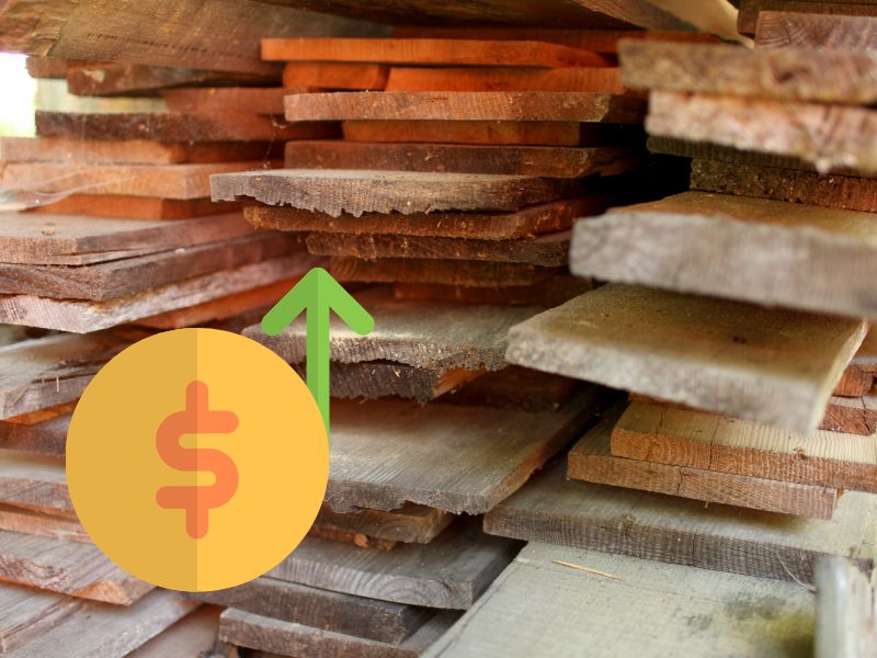 Stacks of planks of reclaimed wood in a lumber yard. In the lower left of the photograph is a yellow dollar symbol with a green arrow pointing upwards.