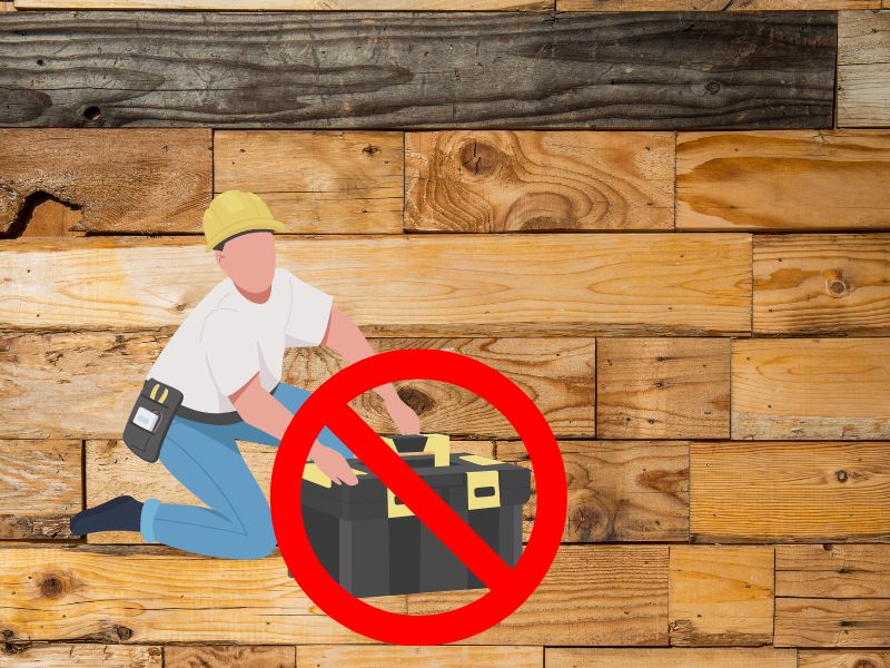 A photograph of reclaimed wood planks with a cartoon workman wearing blue jeans, a white T-shirt, and a yellow hard hat. He is kneeling to open his toolbox, but the toolbox has a red "no entry" symbol across it, indicating no maintenance is required.