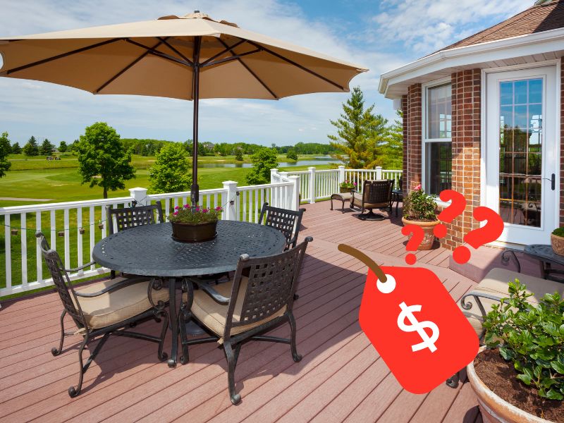 A beautiful brown elevated composite deck is used as an outdoor eating area with circular tables with a parasol and ornate chairs. The edge of the deck is enclosed with white railings and the whole area overlooks manicured lawns. In the lower right corner of the photograph is a red price tag icon with a white dollar sign on it and red question marks above.